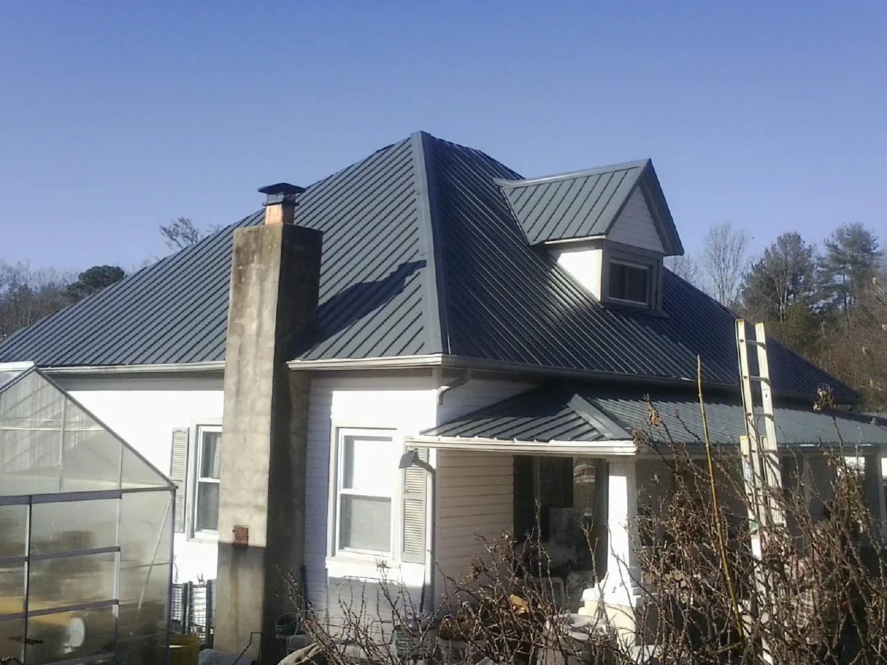 Dark blue standing seam metal roof on a white farmhouse with dormer — Slate & Tile Roof Repair by Roofing Brothers in Clymer