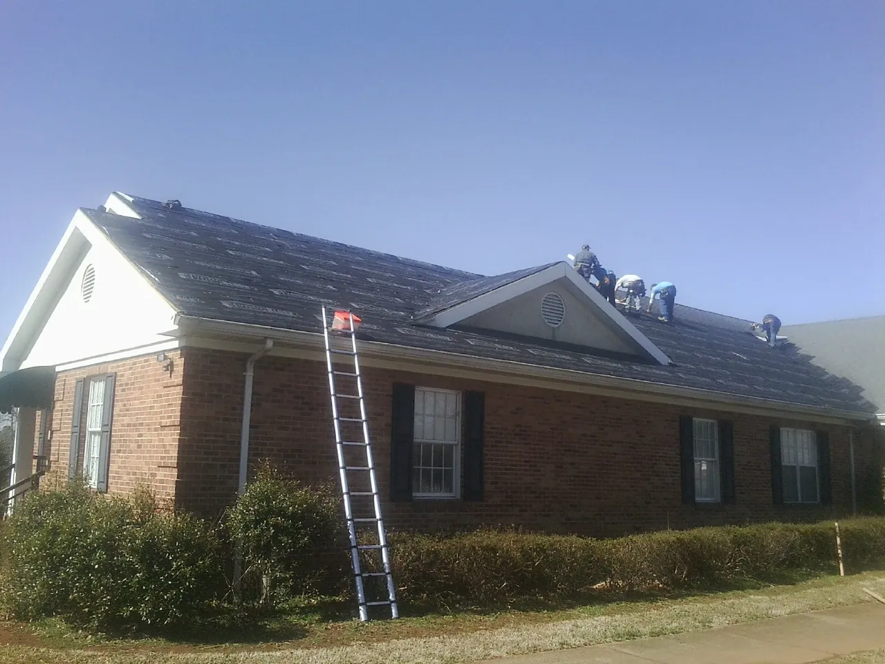Crew tearing shingles off a brick ranch roof with a ladder set — Emergency Roof Repair work by our crew in Clymer