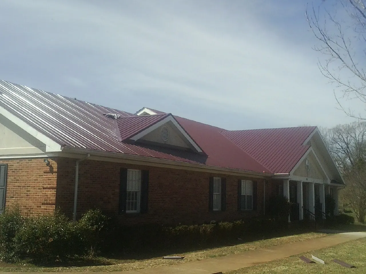 Red metal roof with gabled entries on a long brick building, from a Hail Damage Roof Repair job in Clymer