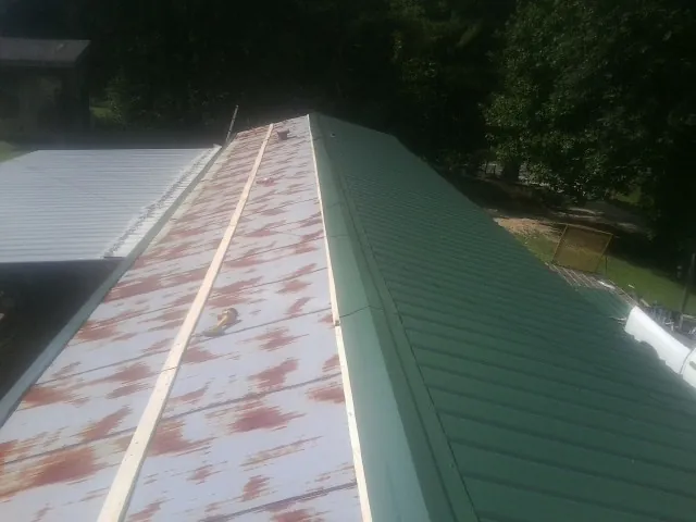 Old rusted panels beside newly installed green metal roofing — Wind Damage Roof Repair by Roofing Brothers in Clymer