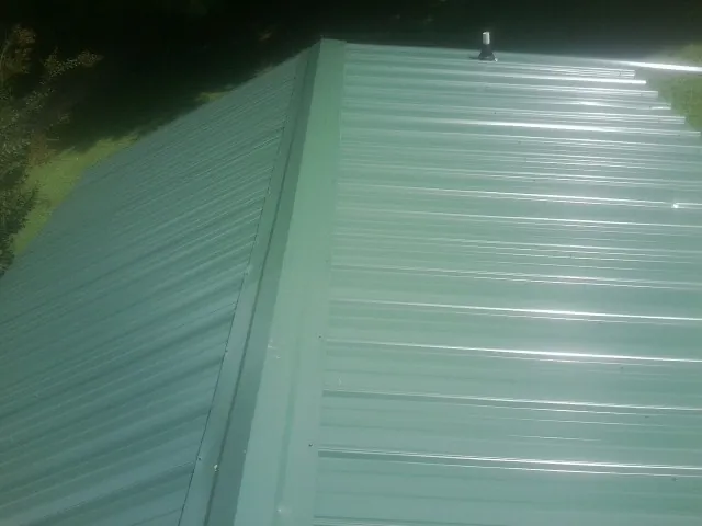 New green metal panels meeting at the ridge of a roof — Flat Roof Repair work by our crew in Clymer