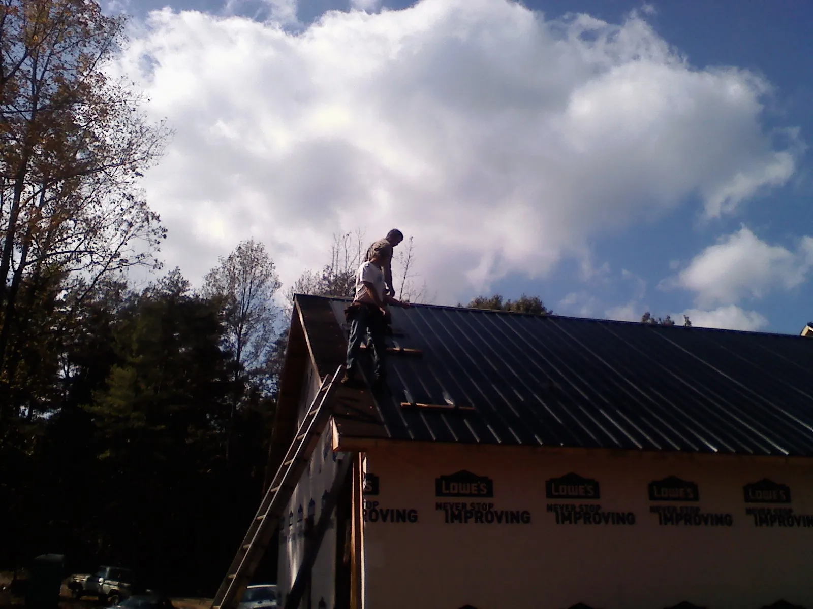 Roofer fastening dark metal panels high against a cloudy sky, from a Roof Inspection job in Clymer