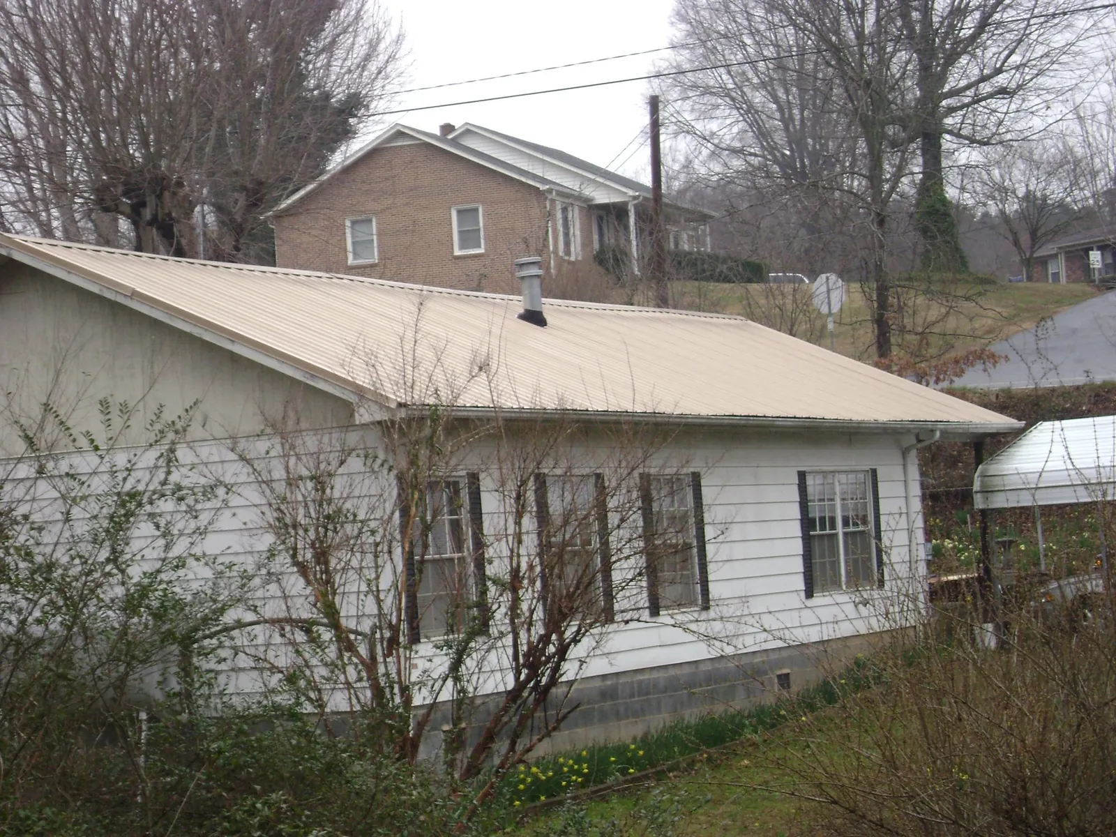 Tan metal roof on a white sided house set into a hillside — Commercial Roofing by Roofing Brothers in Clymer