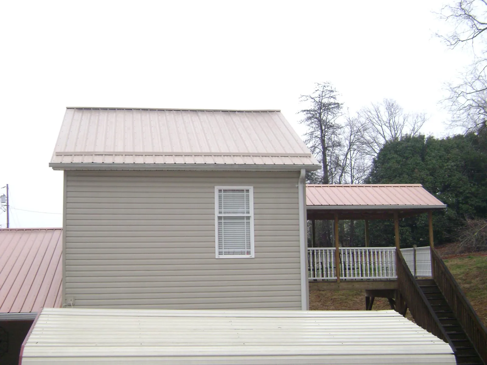 Tan metal roofs on a two story addition and attached porch, from a Roof Replacement job in Clymer